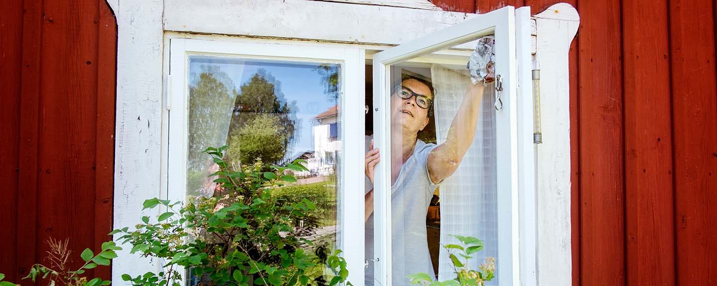 Kvinna som tvättar fönstren i faluröd stuga