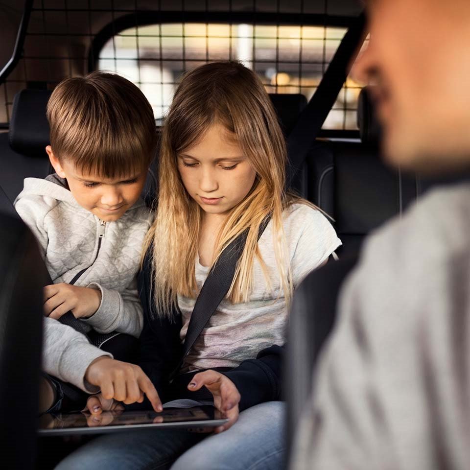 En flicka och en pojke leker med iPad i baksätet på bil