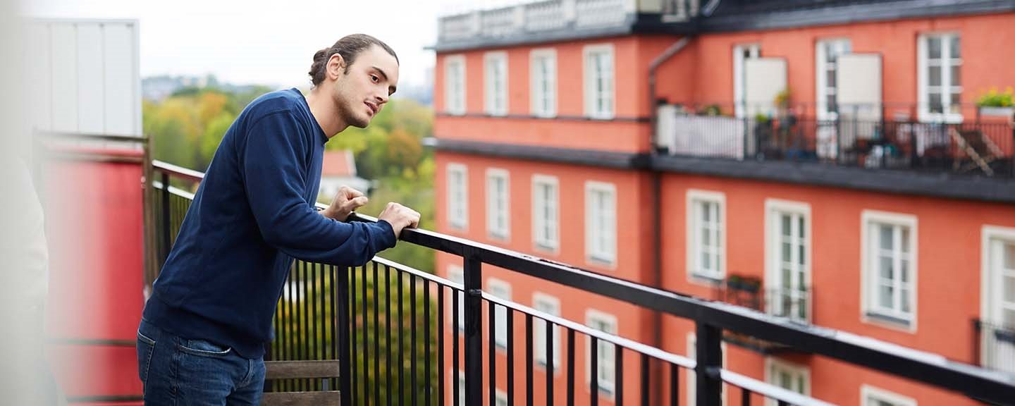 Ung man som står på balkong till lägenhet och tittar ut