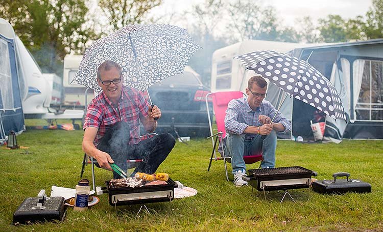 Två män grillar i regn på campingplats