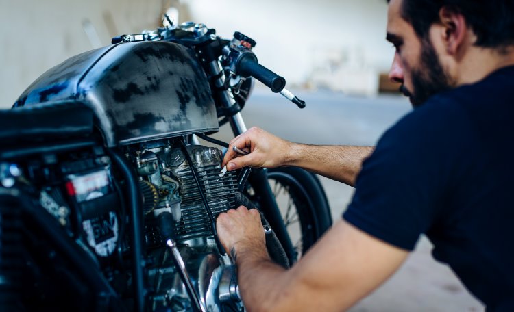 Ung manlig motorcyklist som reparerar vintage motorcykel utomhus