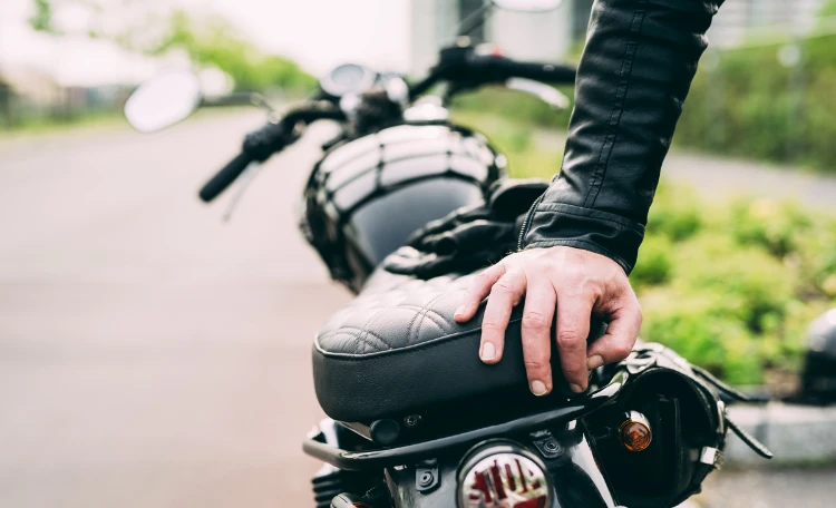 Hand av manlig motorcyklist som lutar sig på motorcykeln