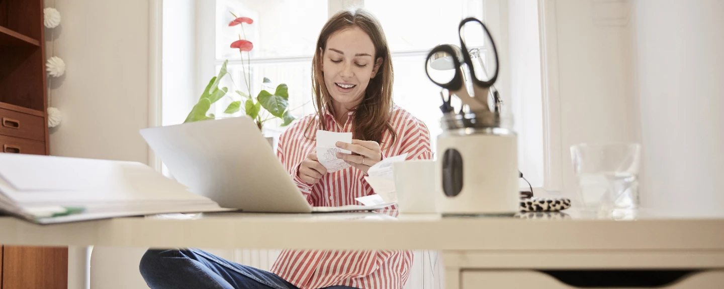 Ung kvinna sitter vid ett skrivbord och tittar ner på en papperslista