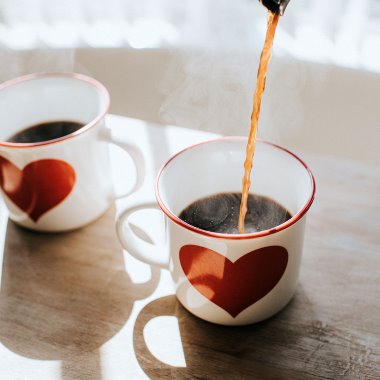 Varmt kaffe hälls upp i två vita kaffekoppar med rött hjärta på