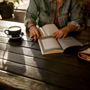 En person sitter vid ett bord med en bok och anteckningsblock framför sig