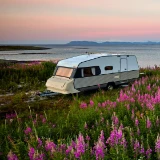 Husvagn vid vattnet med sommarblomster i förgrunden