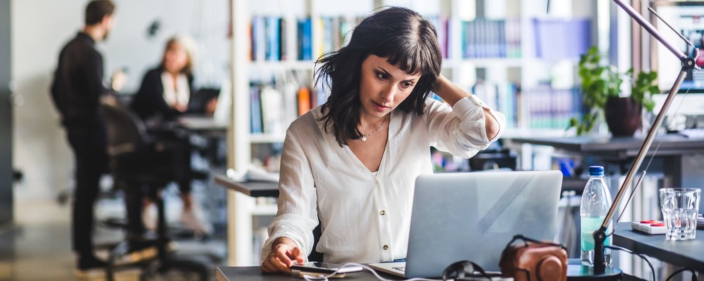 Kvinna i mörkt hår framför laptop på kontor