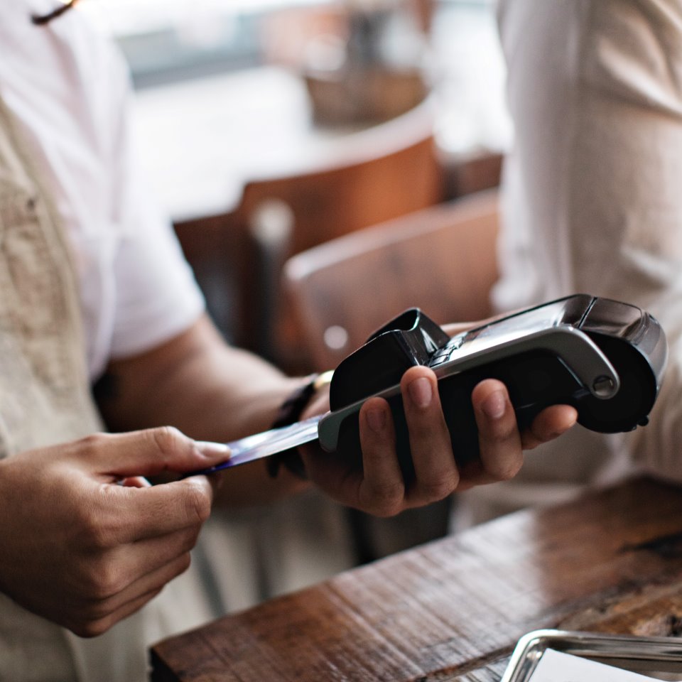 Ägare använder kreditkortsläsare medan han står vid manlig kund vid bordet