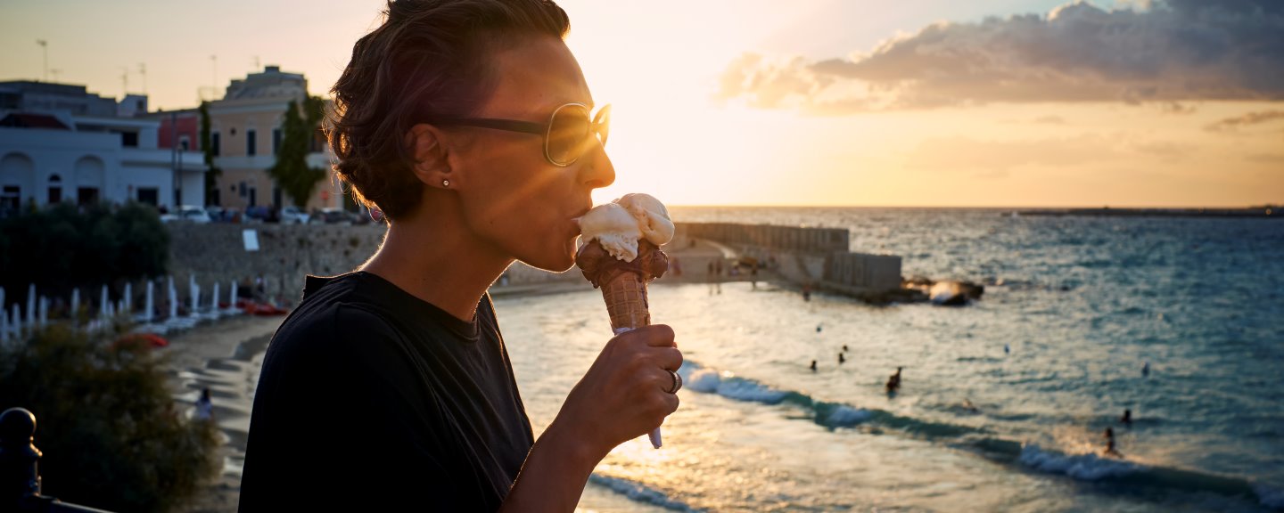 Kvinna med solglasögon äter glasstrut i solnedgång
