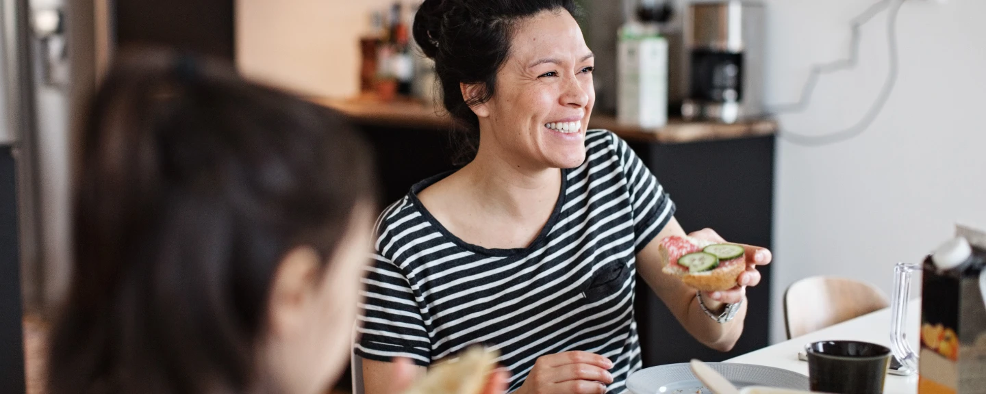 Leende mamma sitter vid köksbordet och äter frukost med sin dotter