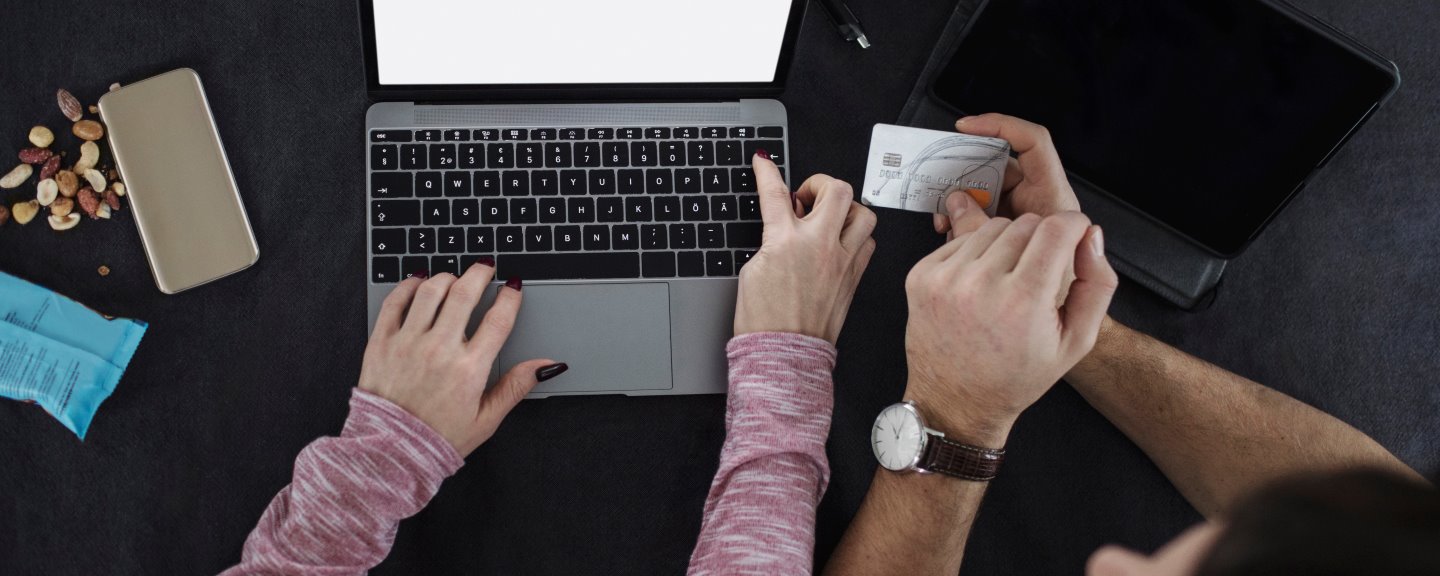 Hög vinkel syn på man som håller kreditkort medan kvinna skriver på bärbar dator.