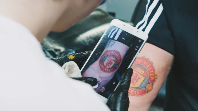 Tatuerare fotar av Nisses tatuering av Manchester United-logotypen med sin mobil.