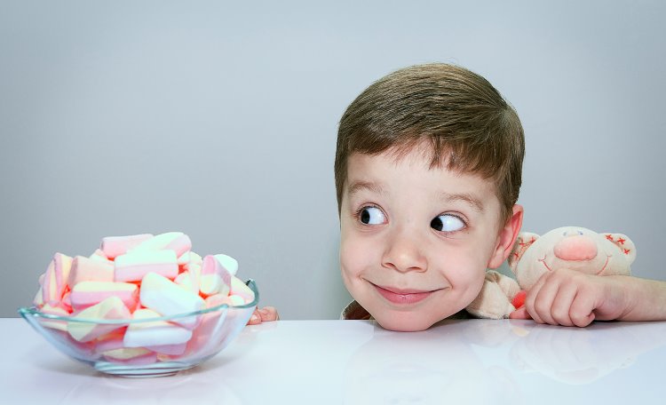 Pojke som kramar gosedjur och tittar intresserat på en skål med marshmallows